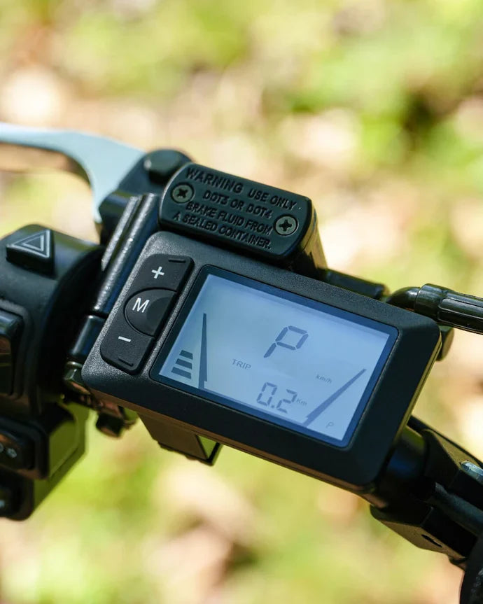 Close-up of the VIPCOO H3 Electric Dirt Bike digital display by Vipcoo, showing speed, trip distance, and various indicators on the handlebar with adjacent buttons and a warning label visible.